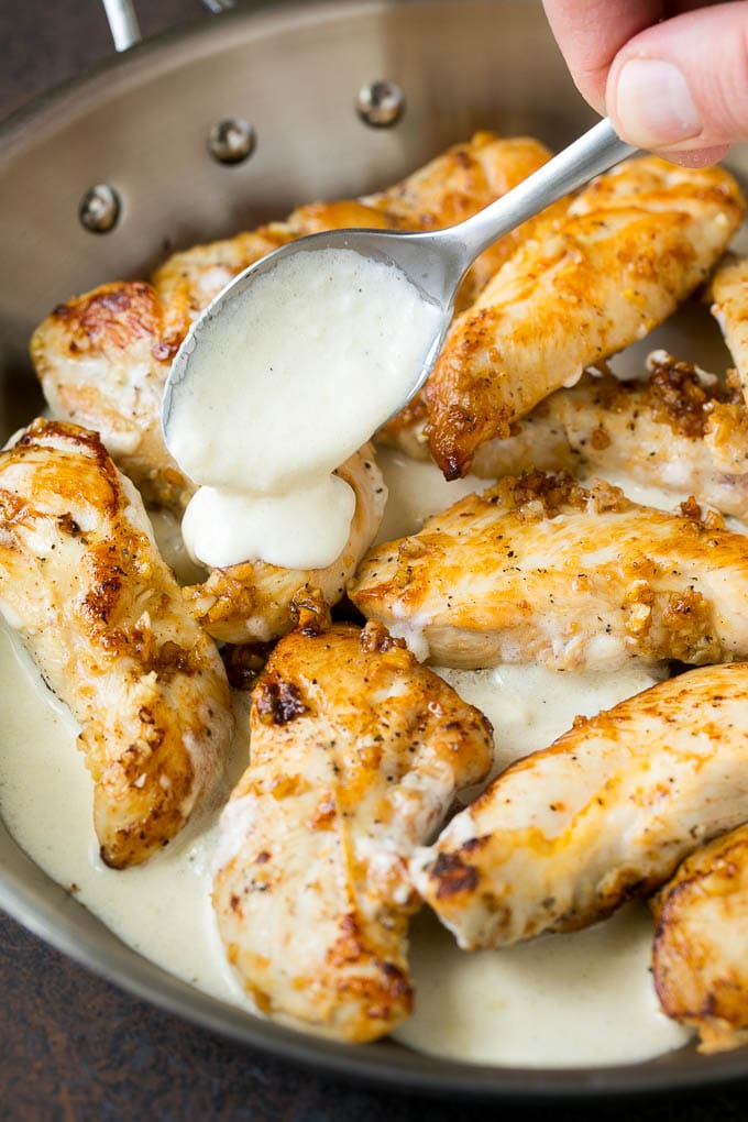 A spoon pouring parmesan cream sauce over garlic chicken.