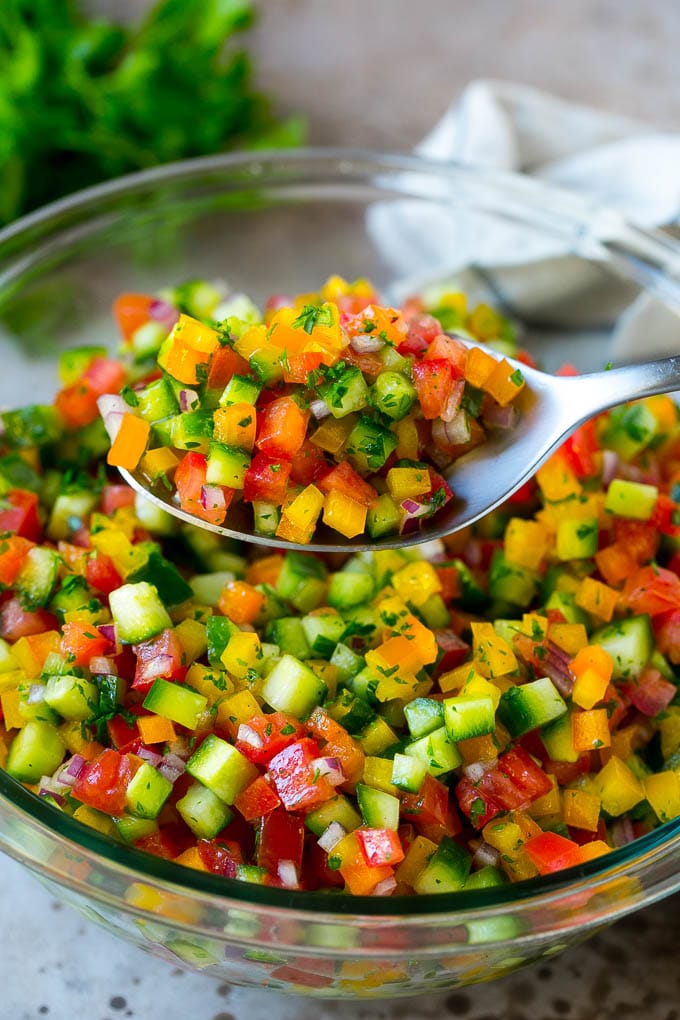 A spoon holding up a serving of Israeli salad.