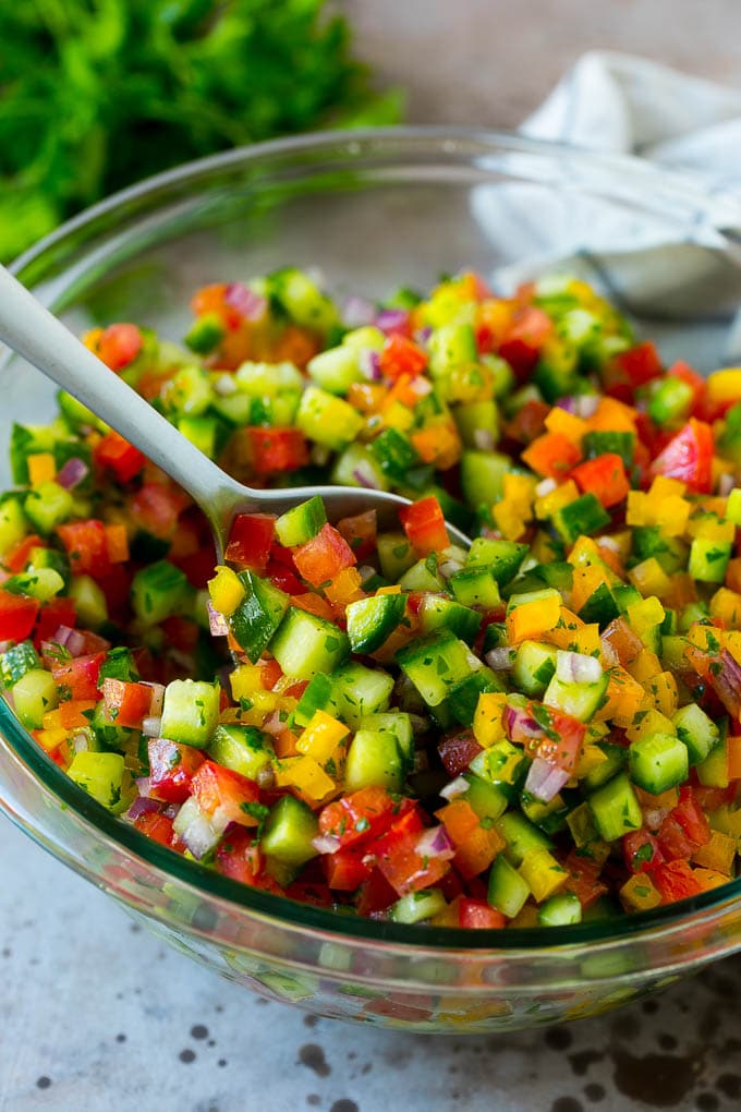 A bowl of Israeli salad with a serving spoon in it.