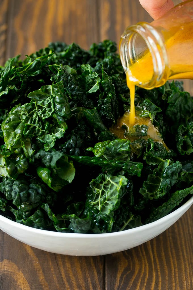 Dressing being poured over dinosaur kale leaves.