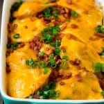 A baked pierogi casserole topped with melted cheese, bacon and green onions.