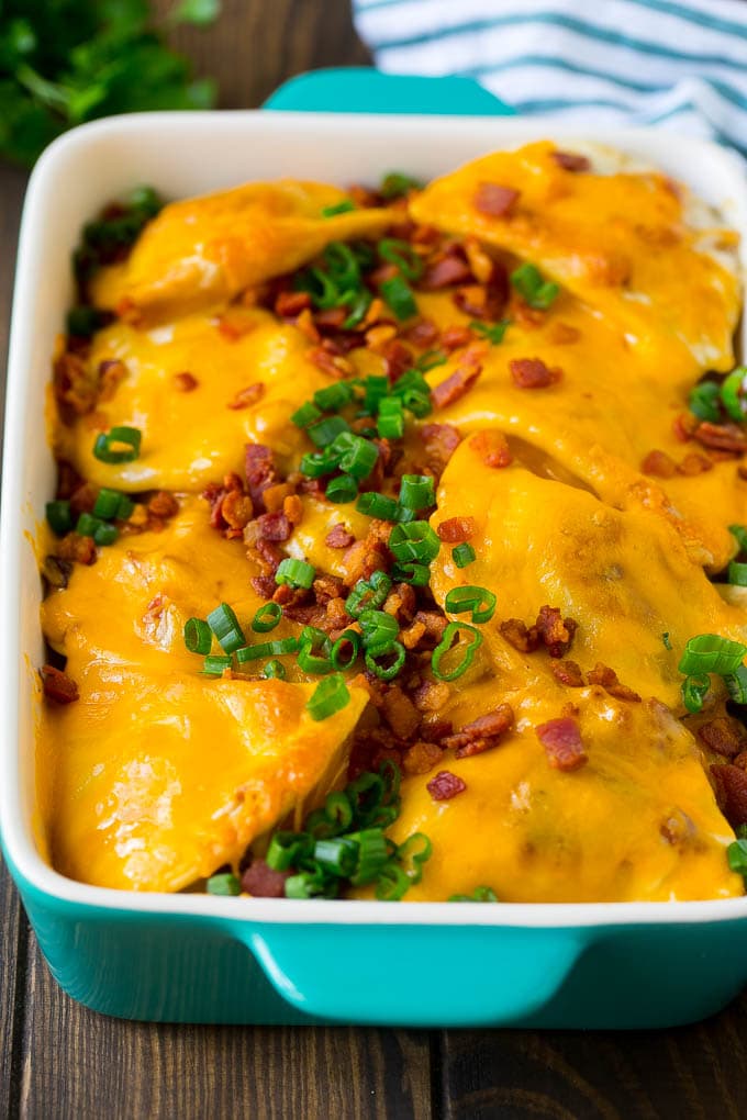 A baked pierogi casserole topped with melted cheese, bacon and green onions.