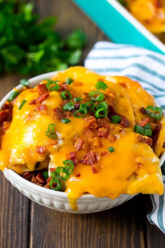 A bowl of pierogi casserole topped with cheddar cheese and bacon.