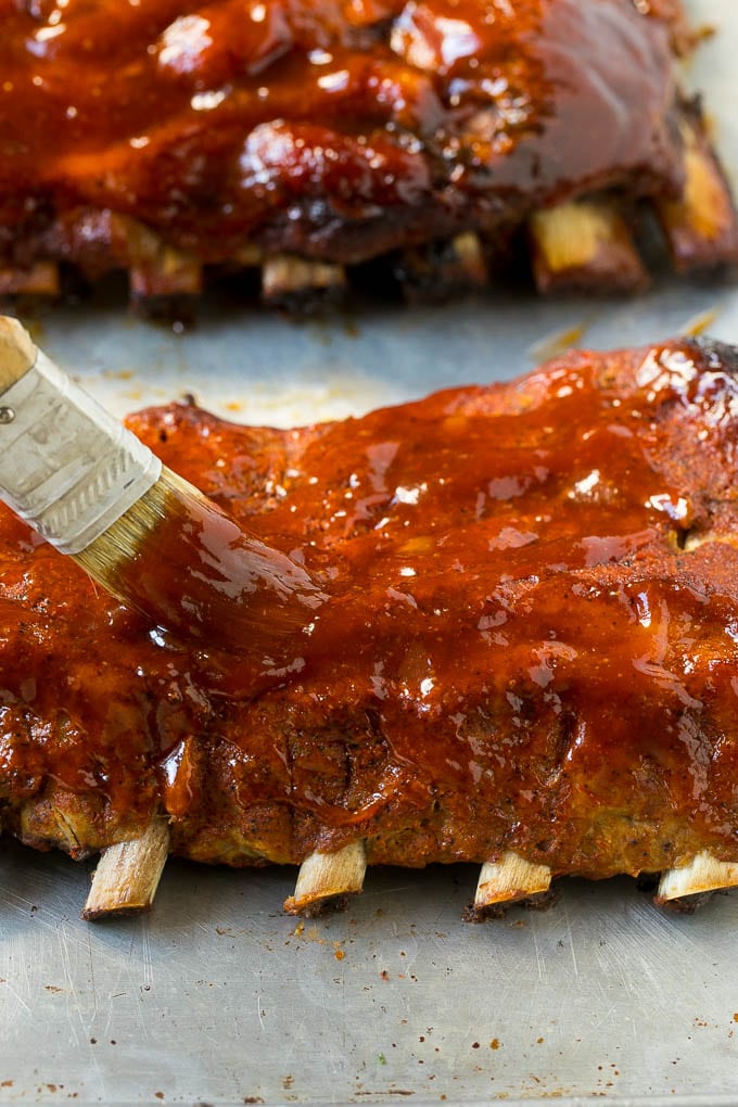 A brush coating cooked pork ribs with BBQ sauce.