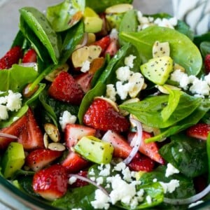 A bowl of strawberry spinach salad with poppy seed dressing, feta cheese and sliced avocado.