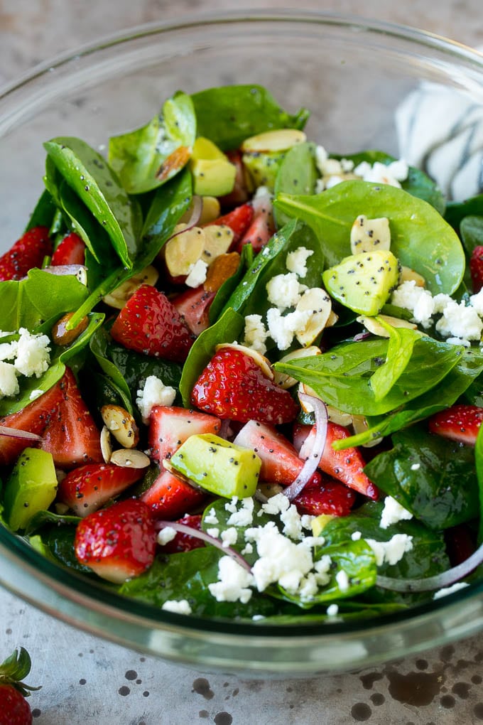 A bowl of strawberry spinach salad with poppy seed dressing, feta cheese and sliced avocado.