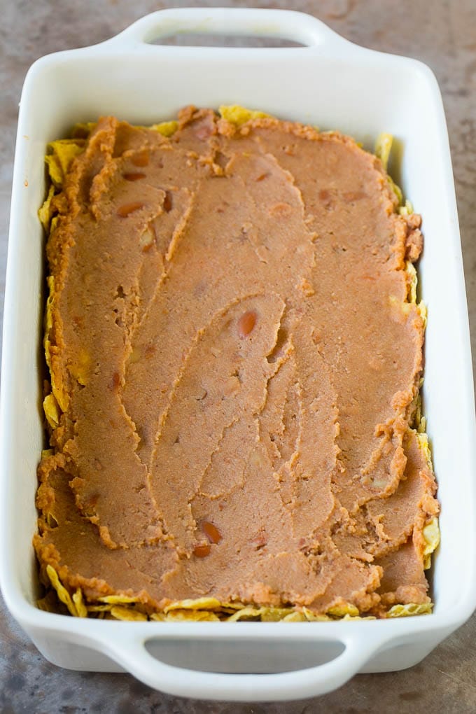 A layer of refried beans on top of a crushed tortilla chips.