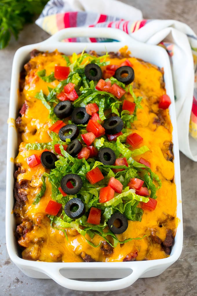 Taco Casserole Recipe | Mexican Casserole | Beef Casserole #casserole #tacos #beef #dinner #cheese #dinneratthezoo Taco casserole in a baking dish topped with melted cheese, lettuce, tomato and olives.