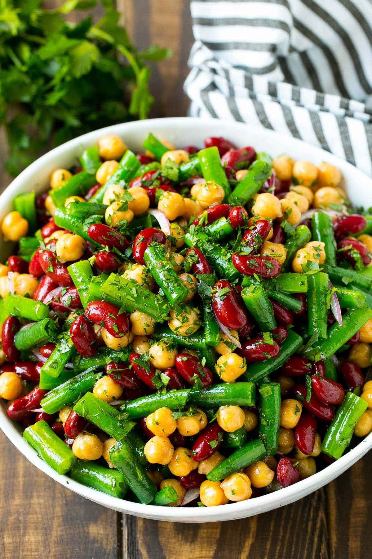 A bowl of three different types of beans topped with dressing and parsley.