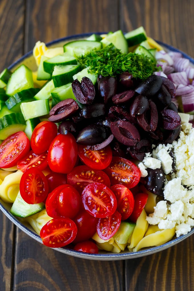 Tortellini in a bowl topped with olives, tomatoes, cucumber and feta cheese.