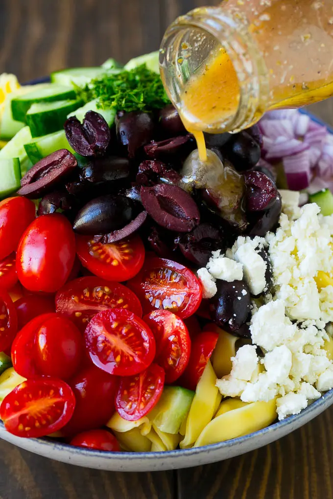 Salatdressing hældes over en skål med tortellini og grøntsager.