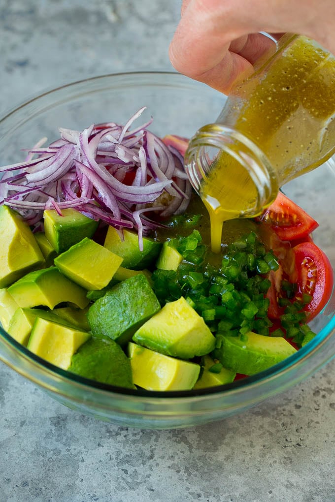 Dressing being poured over avocado, tomato and cilantro.