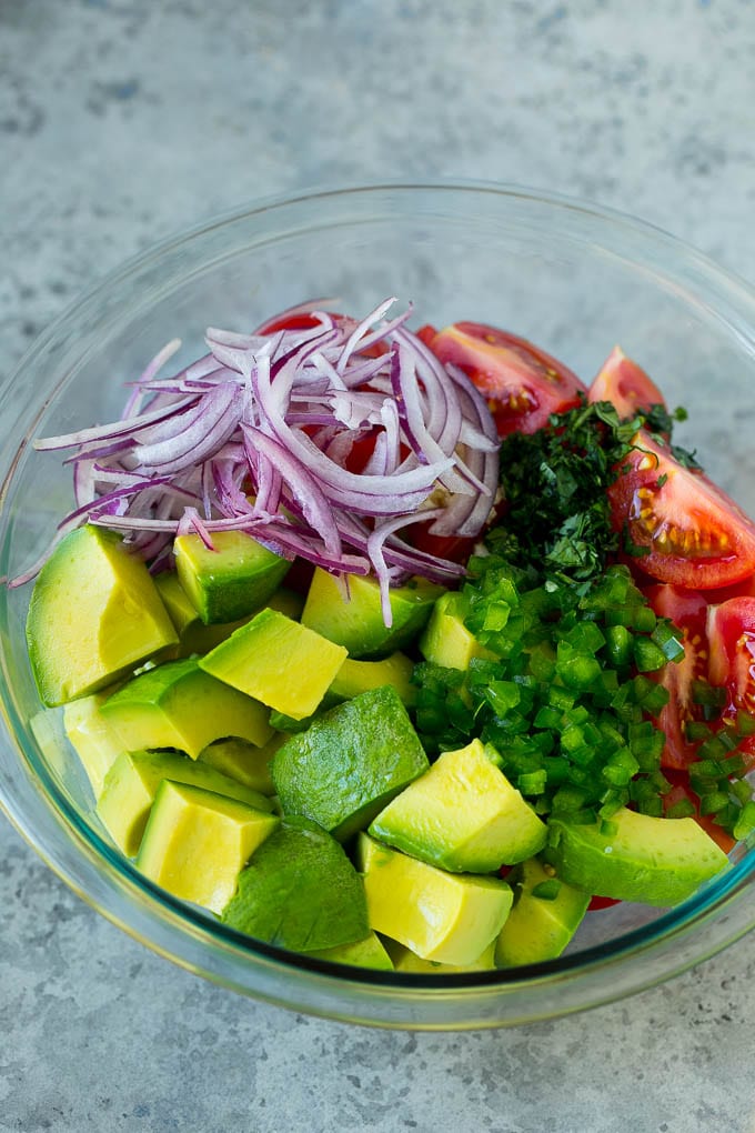 Pieces of avocado, tomato, red onion and minced jalapeno in a salad bowl.