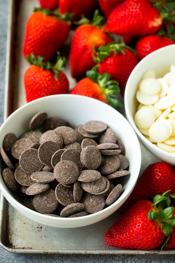 Bowls of dark and white chocolate candy melts surrounded by strawberries.