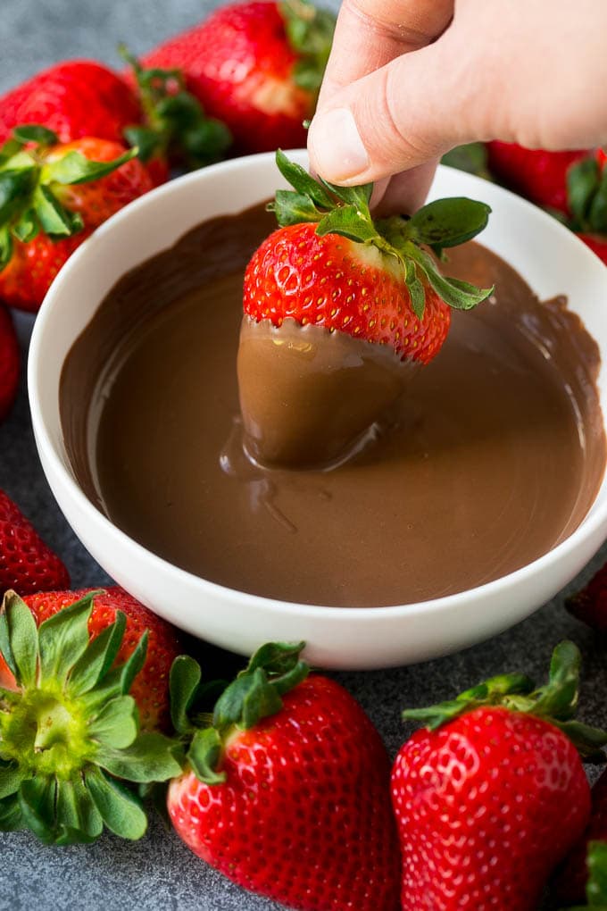 A strawberry being dipped into a bowl of melted chocolate.