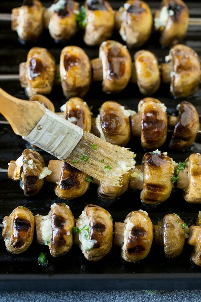 Mushroom kabobs being brushed with garlic butter.