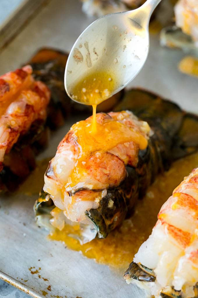 A spoon pouring garlic butter over a lobster tail.