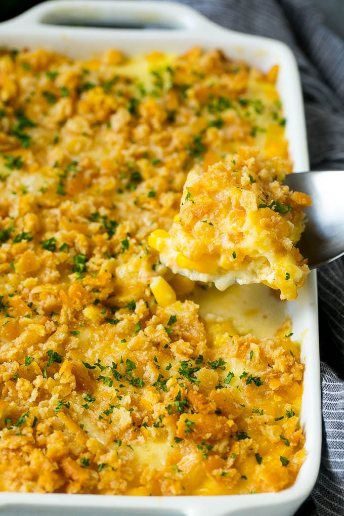 A serving spoon lifting out a portion of scalloped corn.