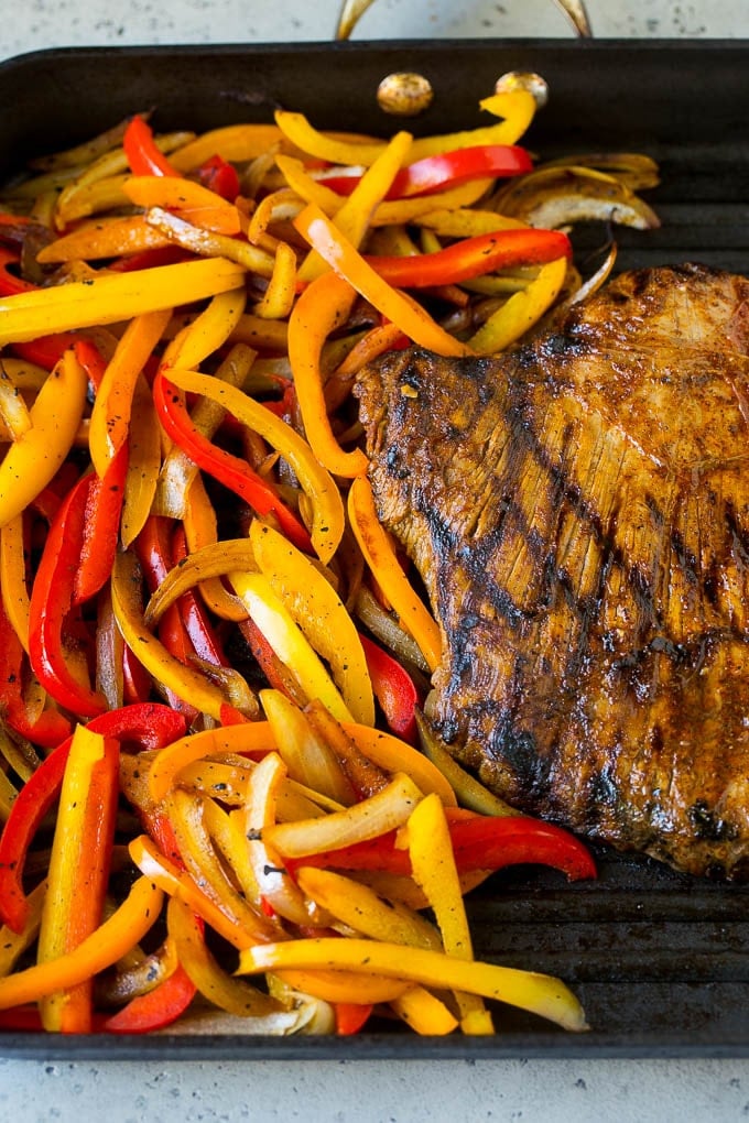 Flank steak and sliced peppers on a grill pan.