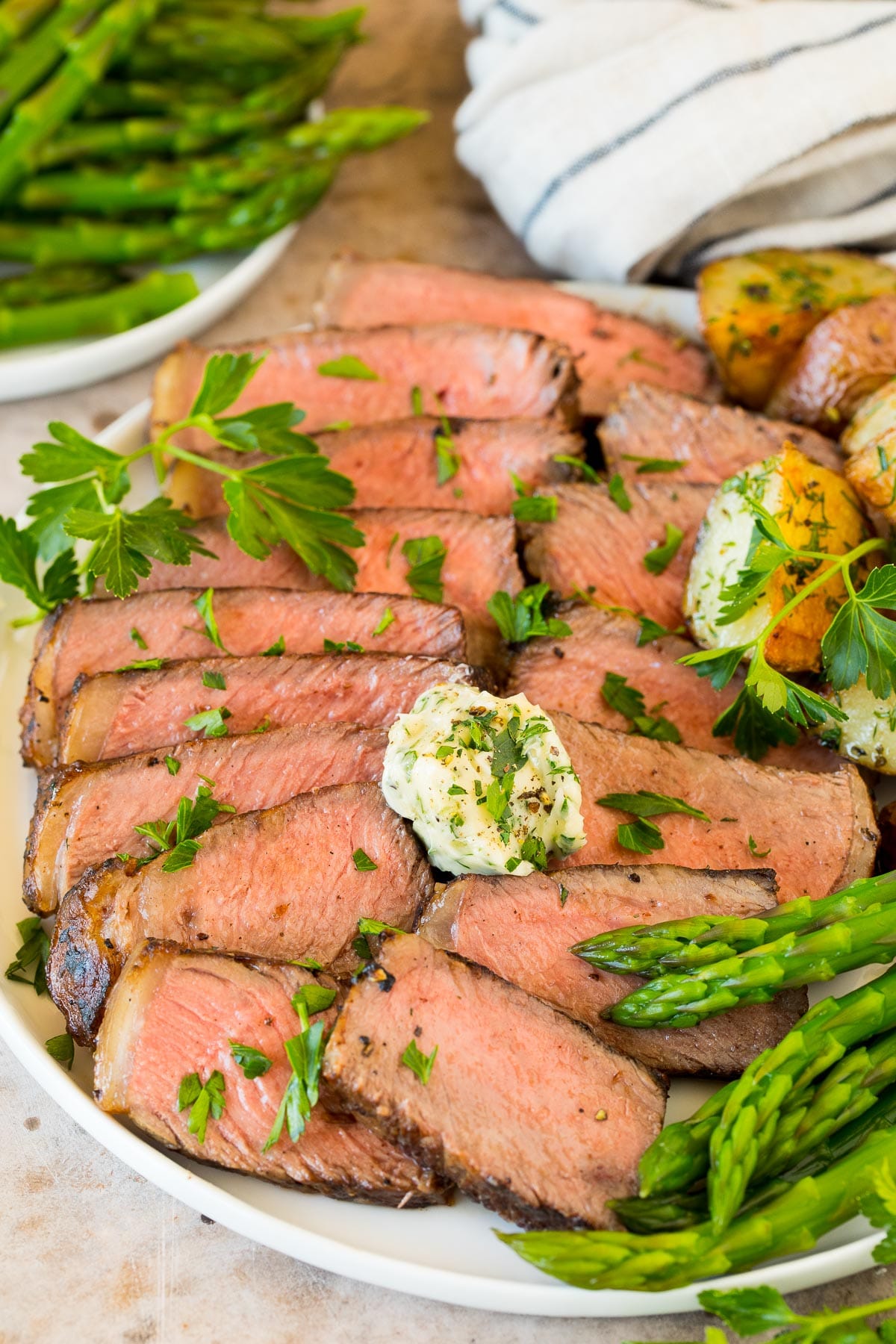 Steak sliced on a platter, topped with herb butter and parsley.