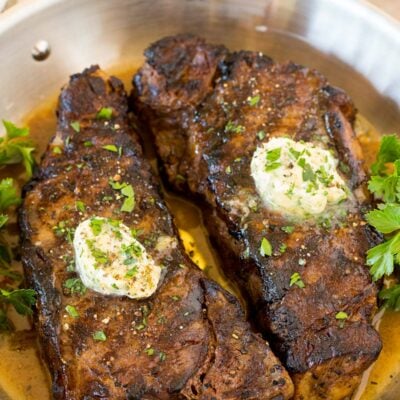 Steaks grilled, sitting in a pan of steak marinade and topped with butter.
