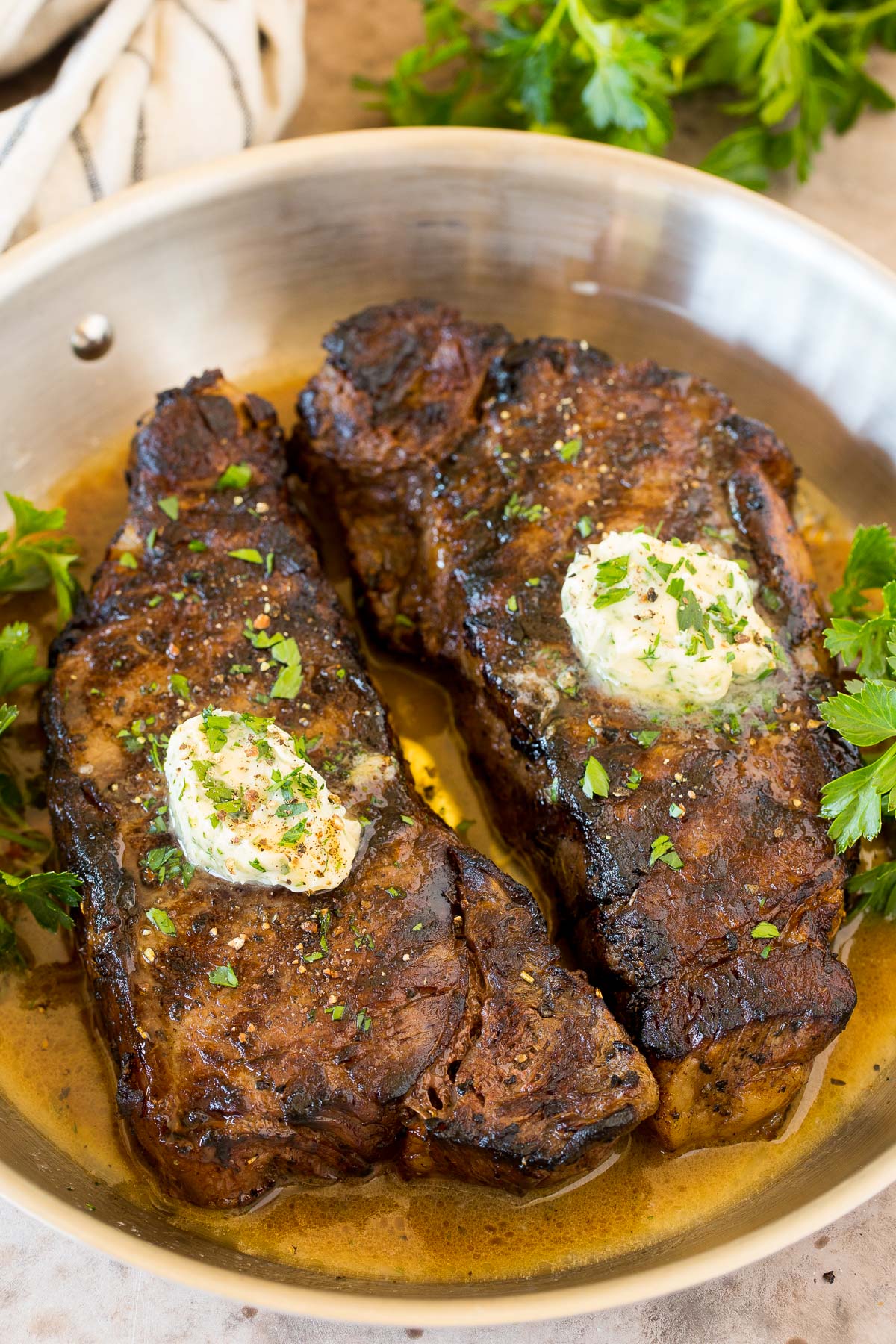Steaks grilled, sitting in a pan of steak marinade and topped with butter.