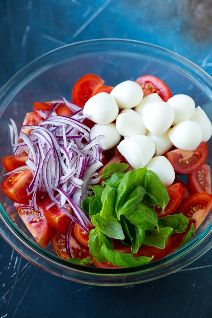 Sliced tomatoes, mozzarella balls, basil and red onion in a bowl.