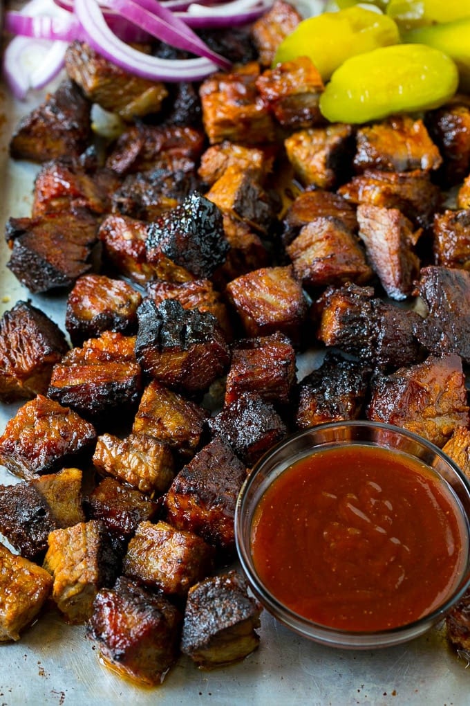 Burnt ends on a sheet pan served with BBQ sauce, red onions and pickles.