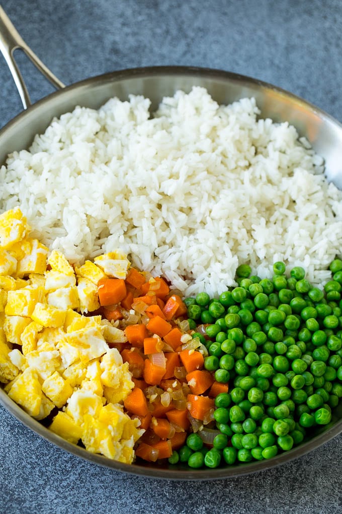 A pan of cooked rice, carrots, eggs and peas.