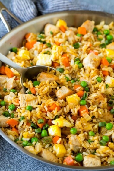 A serving spoon in a pan of chicken fried rice.