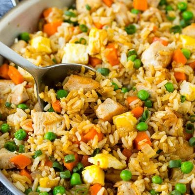 A serving spoon in a pan of chicken fried rice.