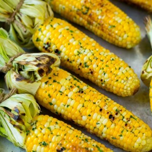 Grilled corn on the cob topped with garlic and herb butter on a sheet pan.
