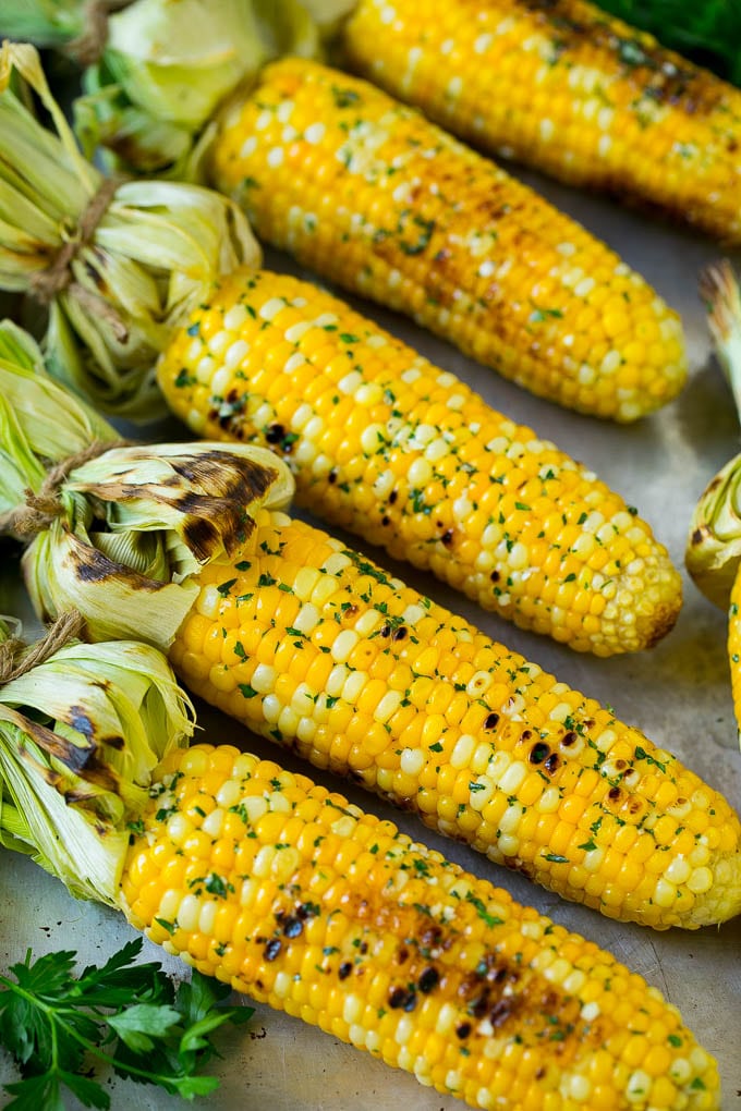 Grilled corn on the cob topped with garlic and herb butter on a sheet pan.