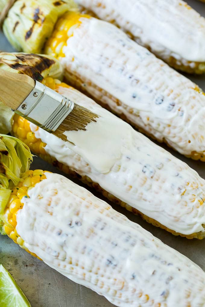 A brush coating corn on the cob with a mixture of mayonnaise and crema.