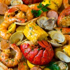 A sheet pan of seafood boil with shrimp, lobster tail, sausage, corn and potatoes.