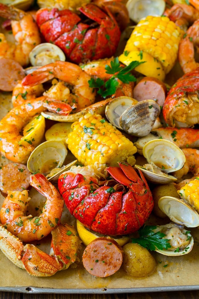 A sheet pan of seafood boil with shrimp, lobster tail, sausage, corn and potatoes.