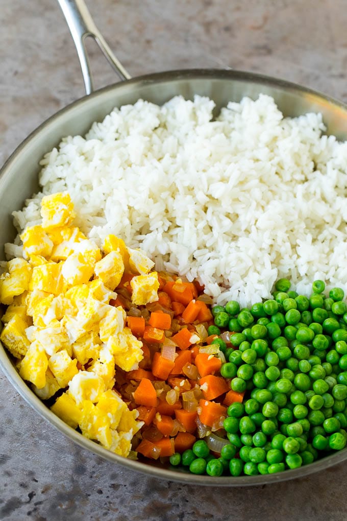 Cooked rice, scrambled eggs, carrots and peas in a pan.