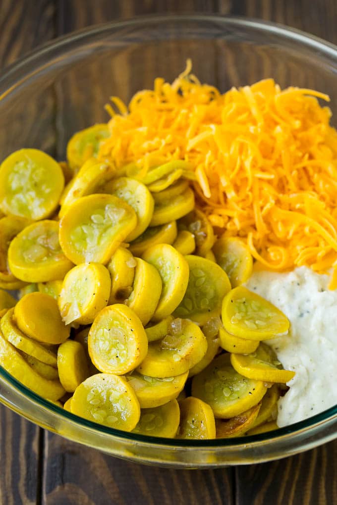 Cooked yellow squash, creamy sauce and cheddar cheese in a mixing bowl.