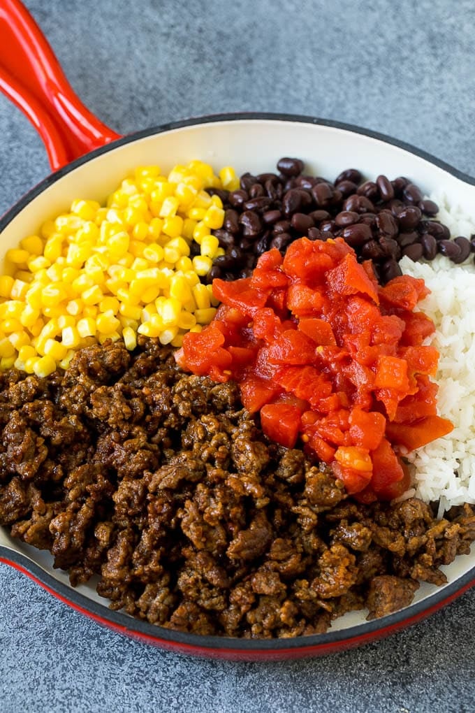 A skillet filled with ground beef, rice, tomatoes, beans and corn.