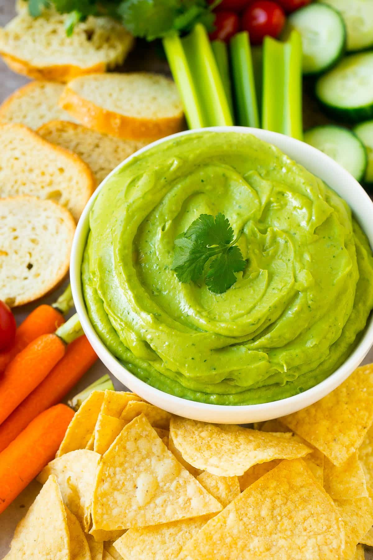 A bowl of avocado dip surrounded by chips and vegetables.