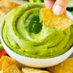 A tortilla chip scooping up a serving of avocado dip.