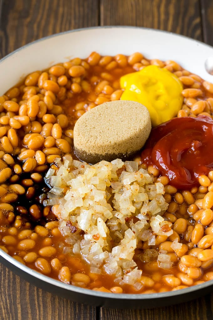 Beans in a pan with onions, molasses, brown sugar, ketchup and mustard.