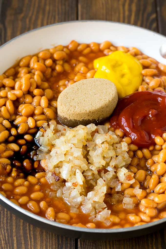 Beans in a pan with onions, molasses, brown sugar, ketchup and mustard.