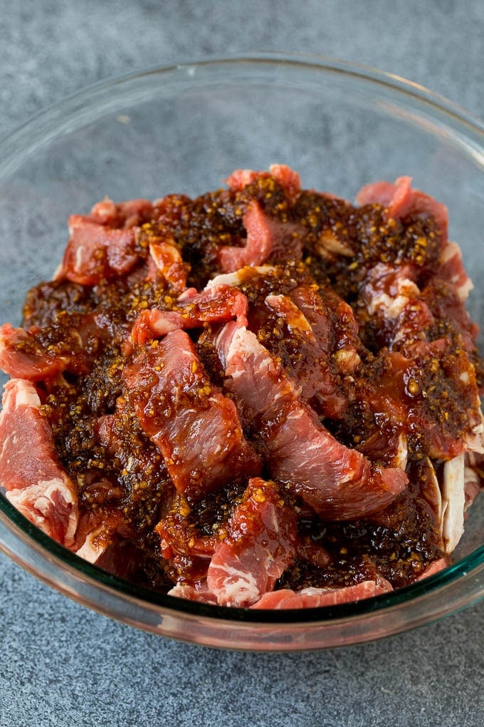 Strips of rib eye in a bowl of marinade.