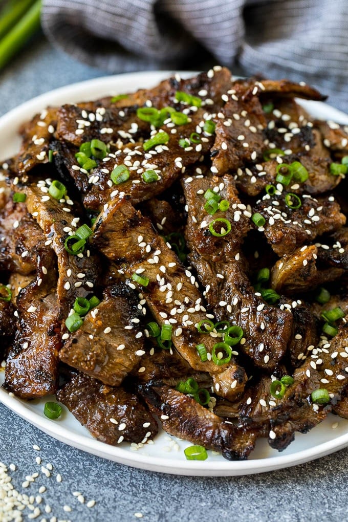 A plate of grilled beef bulgogi topped with sesame seeds and green onions.