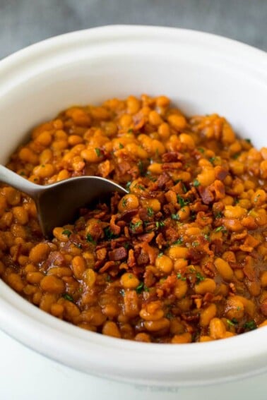 Crock pot baked beans with bacon, with a serving spoon in the pot.