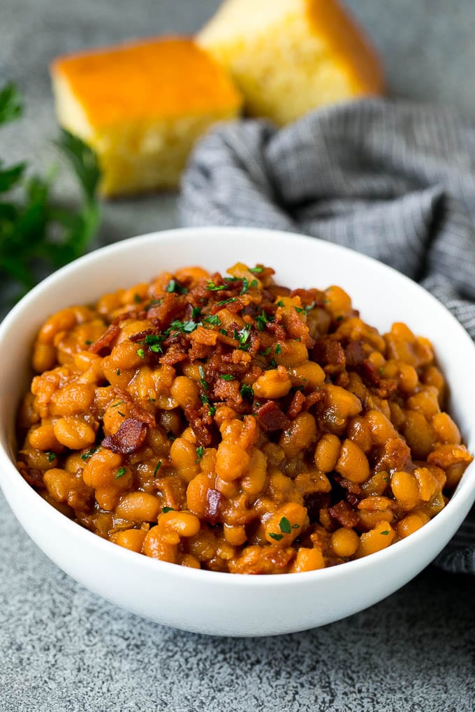 A bowl of crock pot baked beans topped with crispy bacon and served with cornbread.