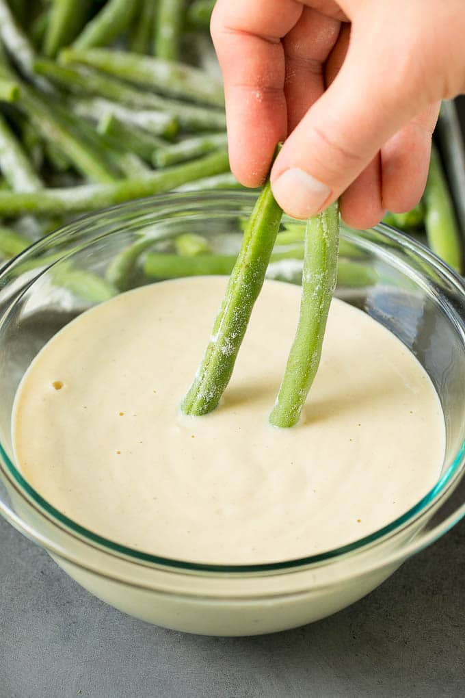 A hand dipping green beans into beer batter.