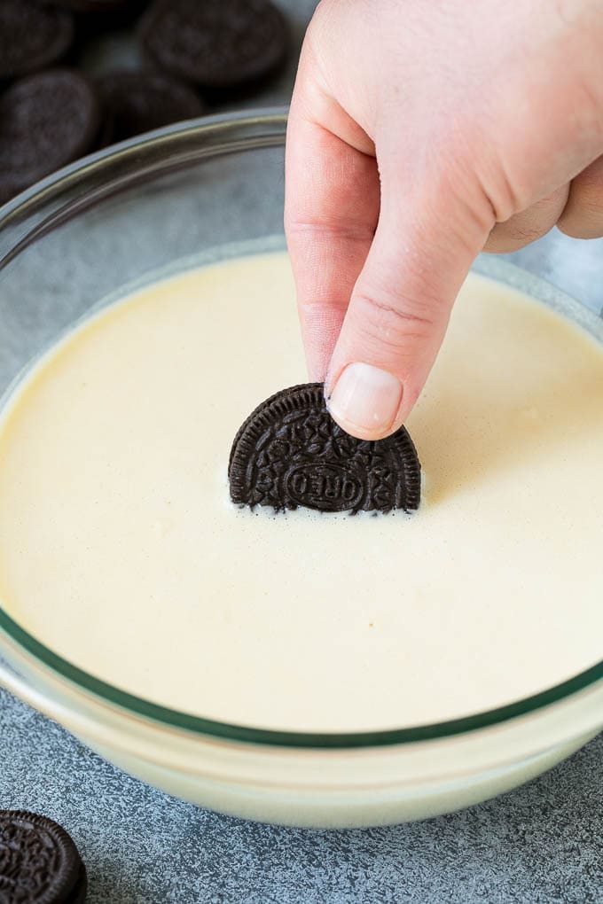 An Oreo cookie being dipped into batter.