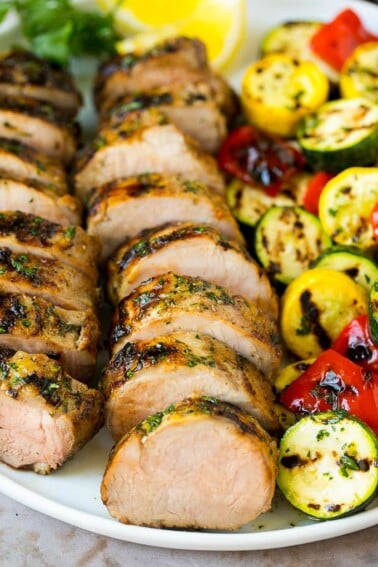 Grilled pork tenderloin on a serving plate with grilled vegetables on the side.